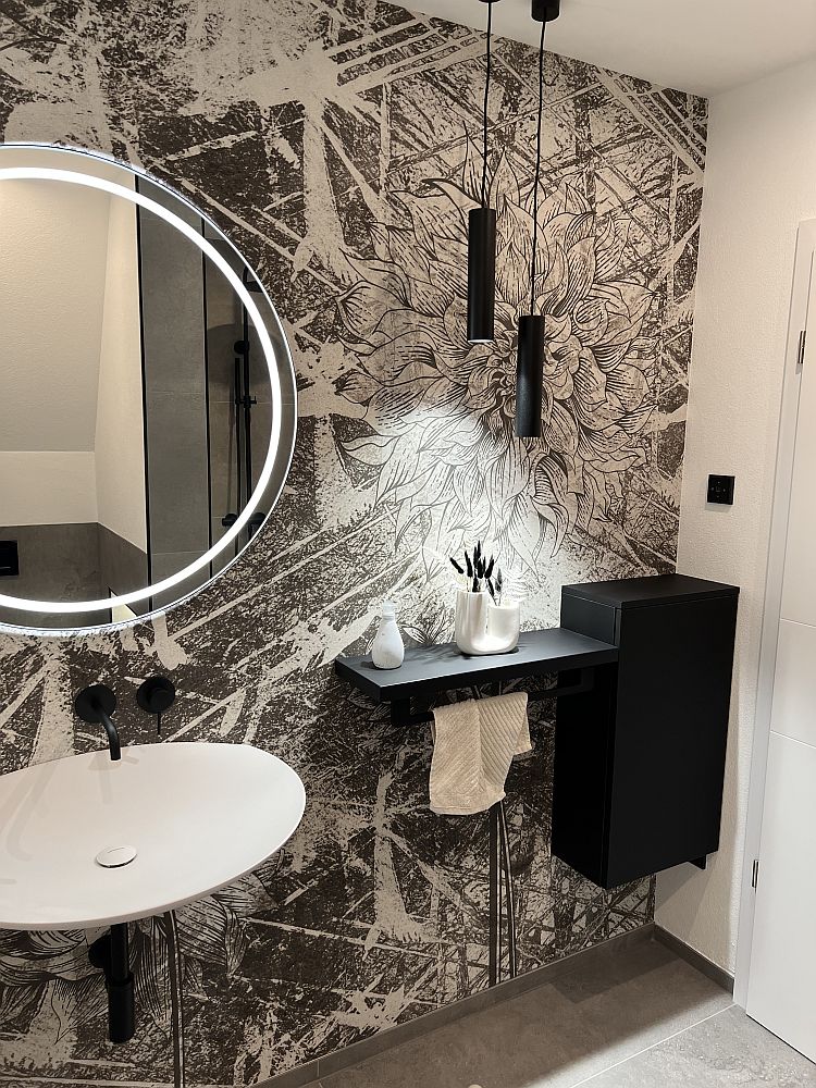 Beleuchtetes Badezimmer mit Motivtapete, Leuchtspiegel und Pendellampen.