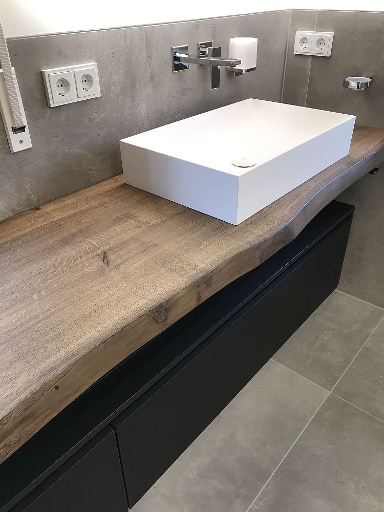 Detailansicht eines massiven Badezimmer-Waschtischs mit Baumkante, schwarzem Unterschrank und einem rechteckigen Aufsatzwaschbecken in modernem Design.