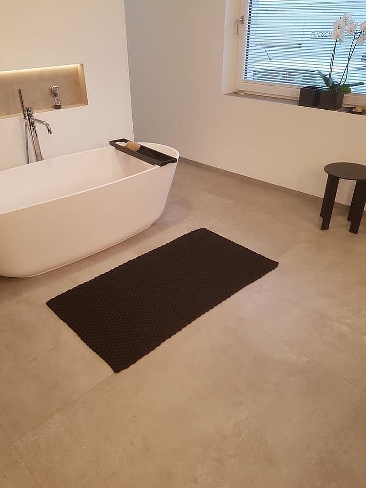Badezimmer mit freistehender Wanne, schwarzem Teppich und kleiner Fensterbank mit Orchidee.