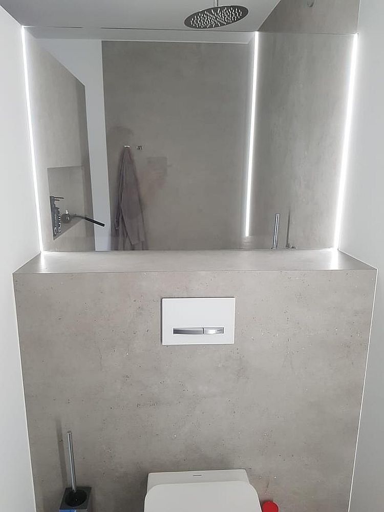 Minimalistisches WC mit Betonwand und silbernem Licht durch vertikale LED-Beleuchtung.