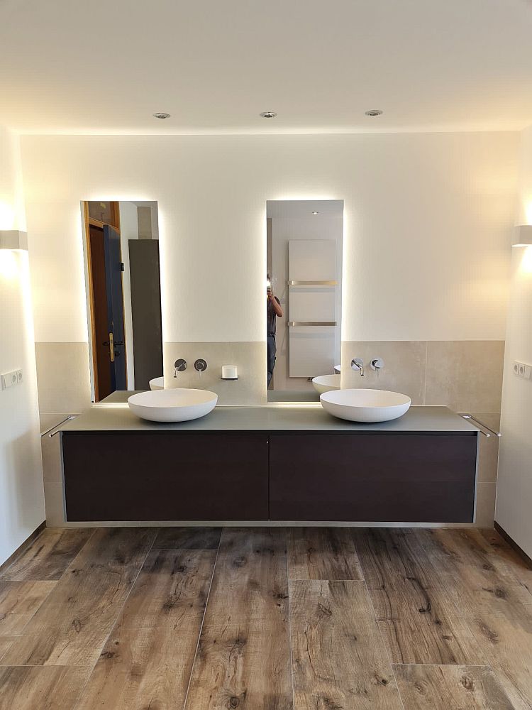 Wandmontierter Waschtisch in dunkler Holzoptik, darauf zwei stilvolle, runde Keramikwaschbecken. Der Boden ist mit hochwertigem Parkett ausgelegt.