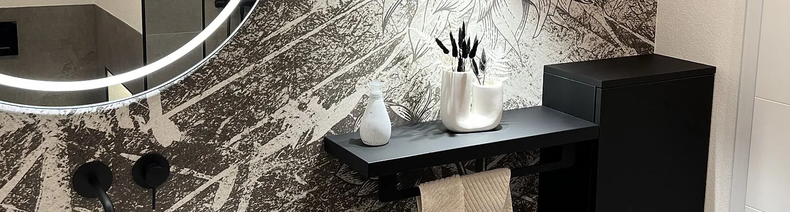 Fensterloses Gästebadezimmer mit Motivtapete, Leuchtspiegel und beleuchteten Regal.
