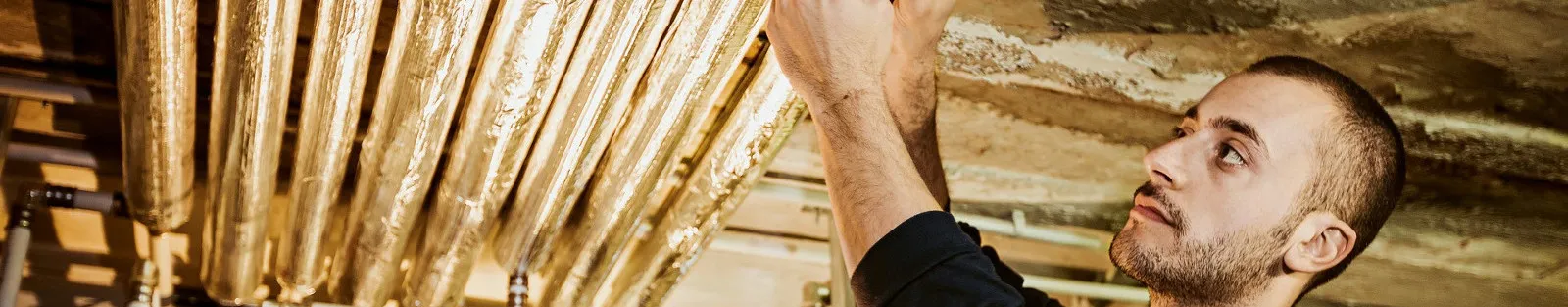 SHK-Anlagenmechaniker beim Isolieren von Heizungsrohren.