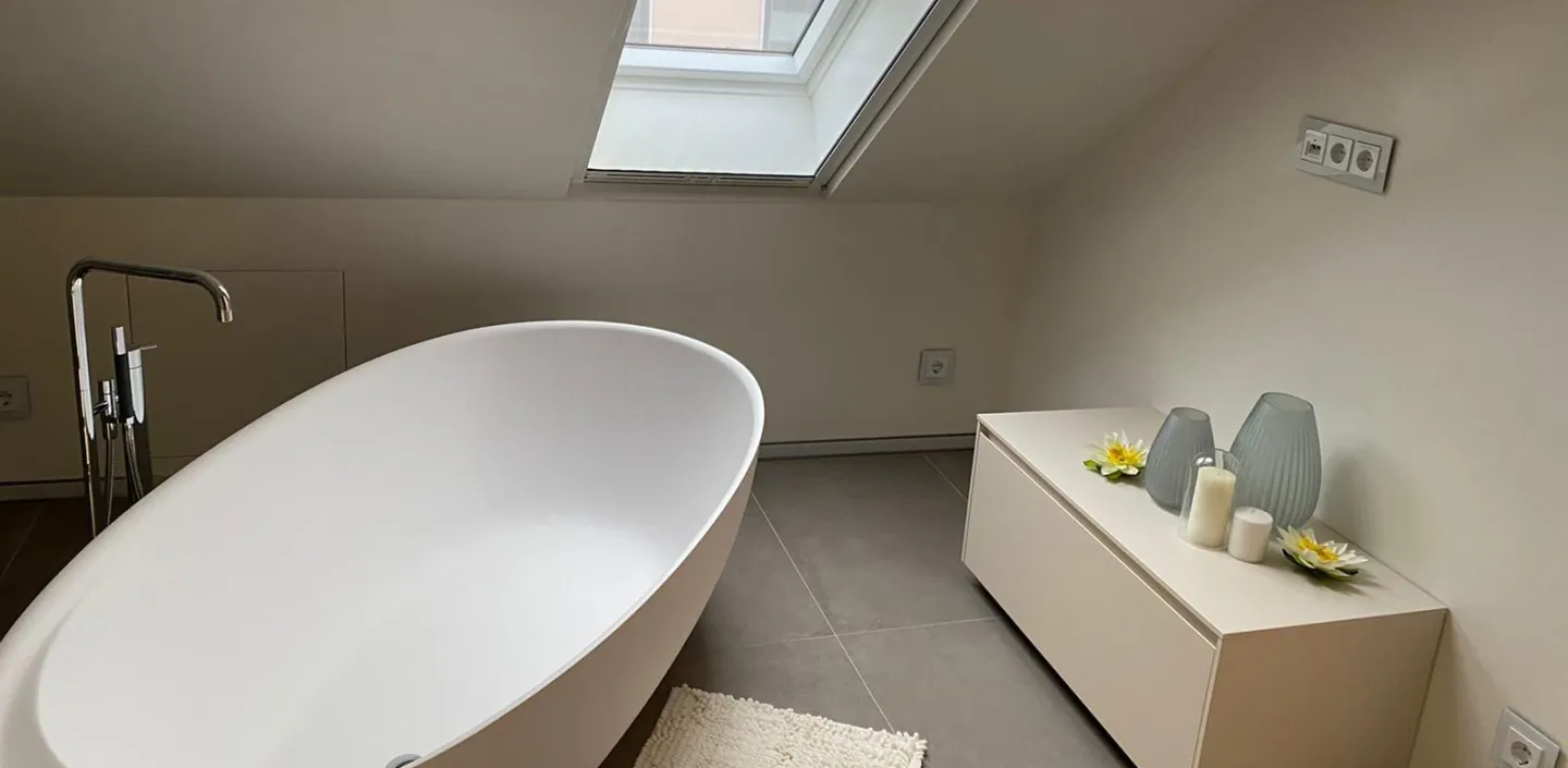 Freistehende Badewanne vor Dachschräge mit Fenster.