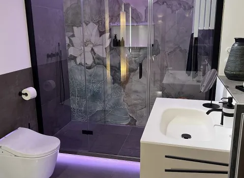 Ein stilvolles Badezimmer mit beleuchteter gläserner Duschkabine, floraler Wandgestaltung und modernen Sanitäranlagen.