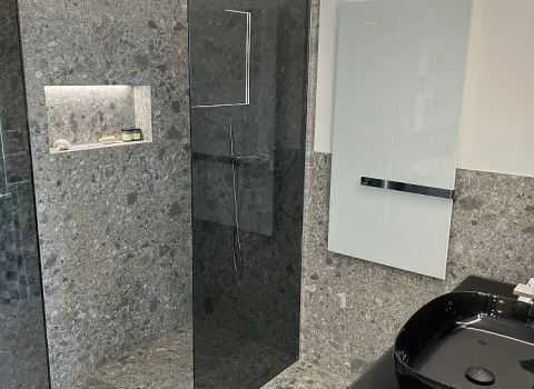 Ein modernes Badezimmer mit grauer Natursteinoptik, einer offenen Walk-in-Dusche und einem schwarzen Designer-Waschbecken.