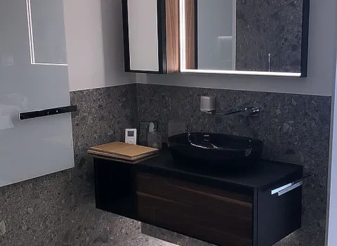 Ein modernes Badezimmer mit schwebendem Waschtisch in Holzoptik, einem schwarzen Aufsatzwaschbecken und einem beleuchteten Spiegel.