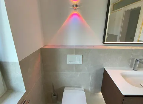 Minimalistisches WC mit hell-beigen Fliesen und rosafarbenem Licht.