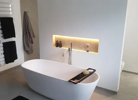 Stilvolle Badewanne mit goldener LED-Nische, Wandarmatur und schwarzem Teppich.