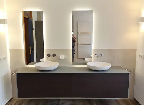 Ein elegantes Badezimmer mit einem wandmontierten Waschtisch in dunkler Holzoptik, darauf zwei stilvolle, runde Keramikwaschbecken. Der Boden ist mit hochwertigem Parkett ausgelegt.