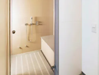 Ein minimalistisches Badezimmer mit einer geräumigen Dusche, die durch eine Glastür betreten wird. Die Dusche ist in einem sanften Beigeton gehalten und verfügt über einen rutschfesten Boden mit integrierten Streifen. 