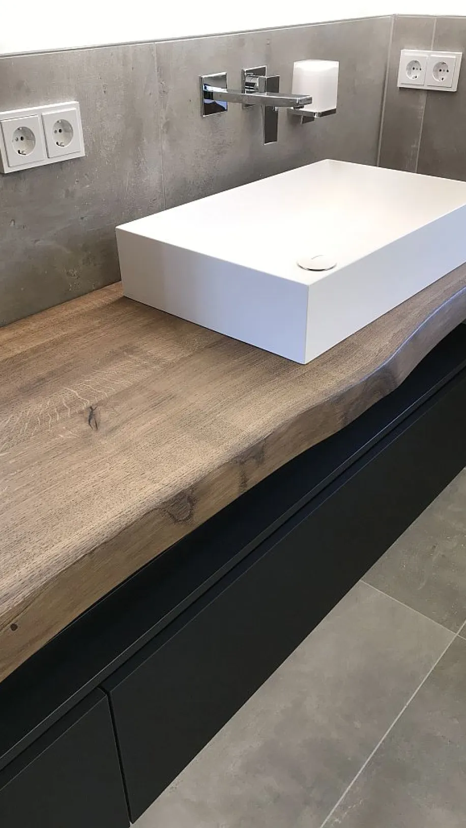 Detailansicht eines massiven Badezimmer-Waschtischs mit Baumkante, schwarzem Unterschrank und einem rechteckigen Aufsatzwaschbecken in modernem Design.