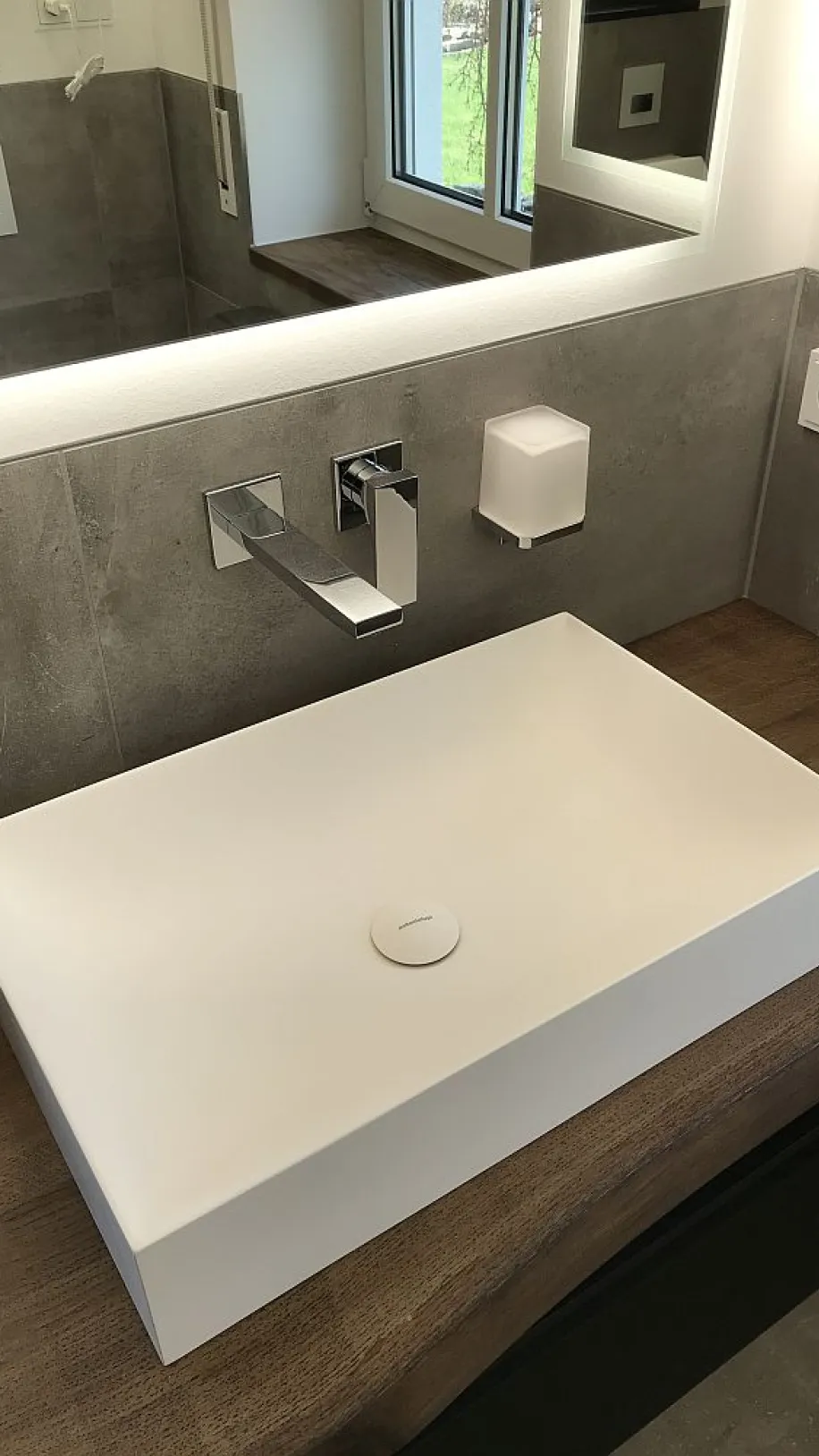 Detailaufnahme eines rechteckigen Waschbeckens im Masterbad, eingebettet in eine edle Kombination aus Holz, grauen Fliesen und modernen Armaturen.