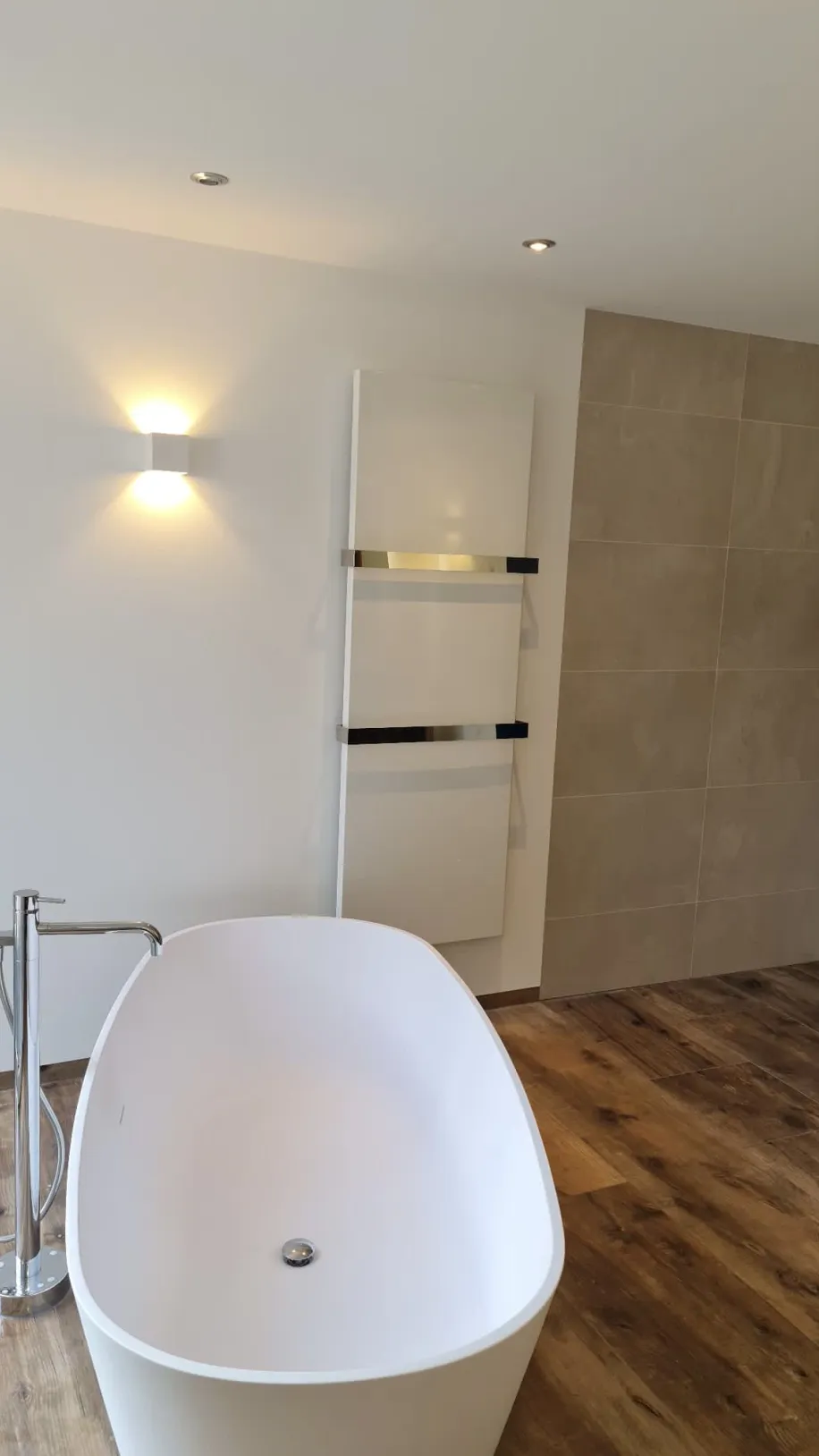 Badewanne mit einer freistehenden Armatur aus Edelstahl. Daneben befindet sich eine bodenebene Walk-in-Dusche.