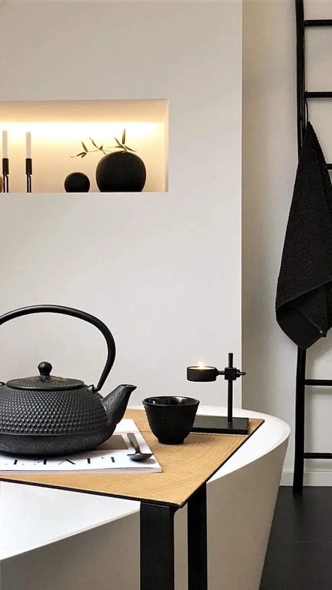 Wohnliches Badambiente mit Tisch mit Guss-Teekanne, beleuchteter Wandnische und Handtuchleiter.