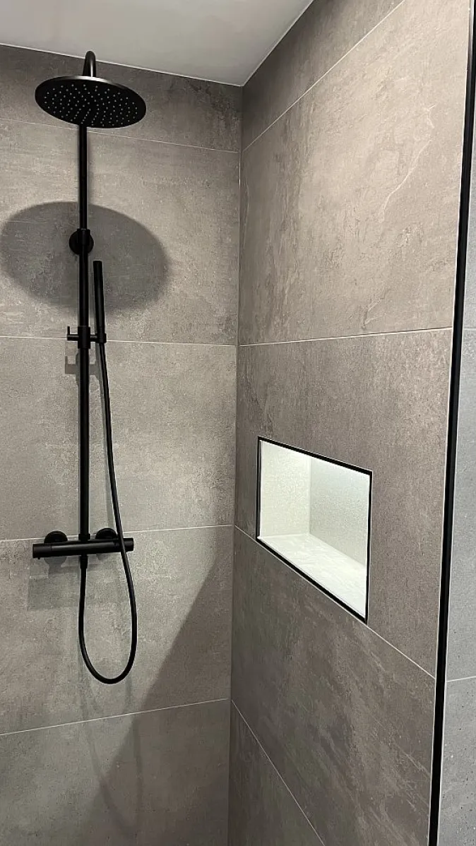 Duschbereich mit schwarzer Aufputzarmatur und beleuchteter Wandnische.