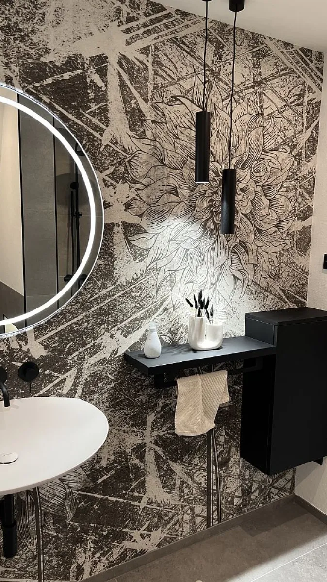 Beleuchtetes Badezimmer mit Motivtapete, Leuchtspiegel und Pendellampen.