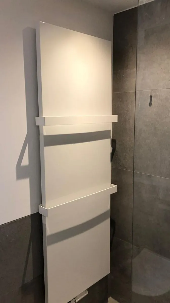 Ein weißer, schlanker Handtuchheizkörper mit klaren Linien ist in einem Badezimmer montiert. 