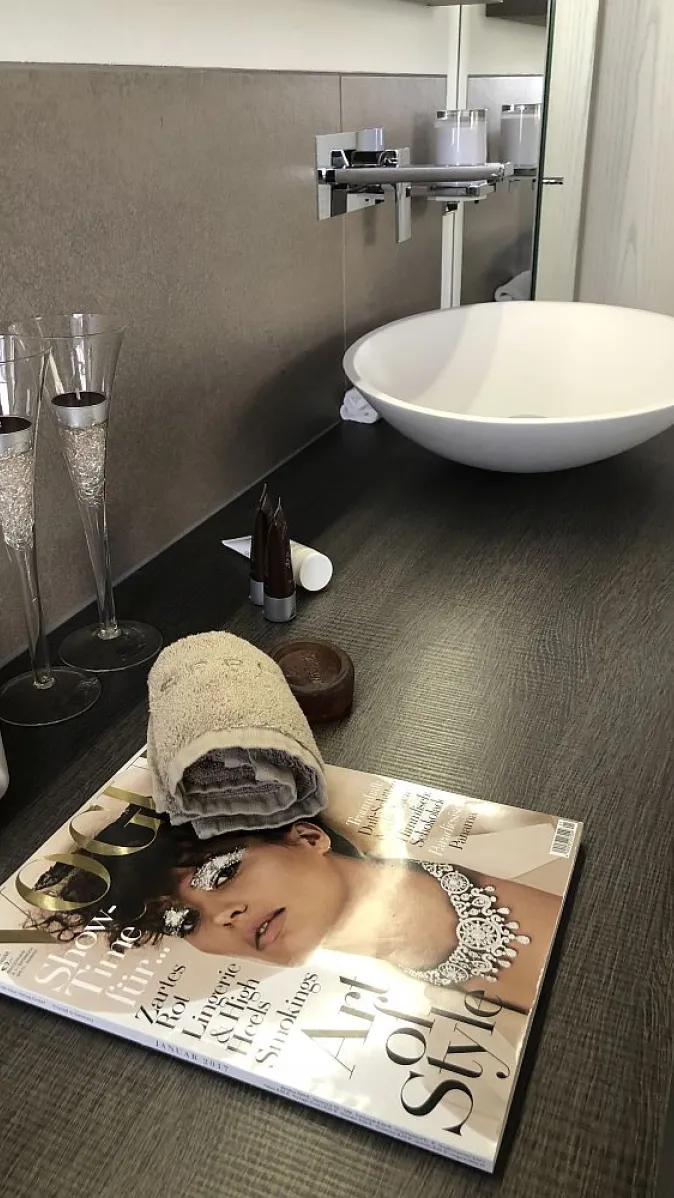 Stilvoll eingerichteter Waschtisch mit Glasdeko, einer gerollten Handtuchrolle und einer Zeitschrift.