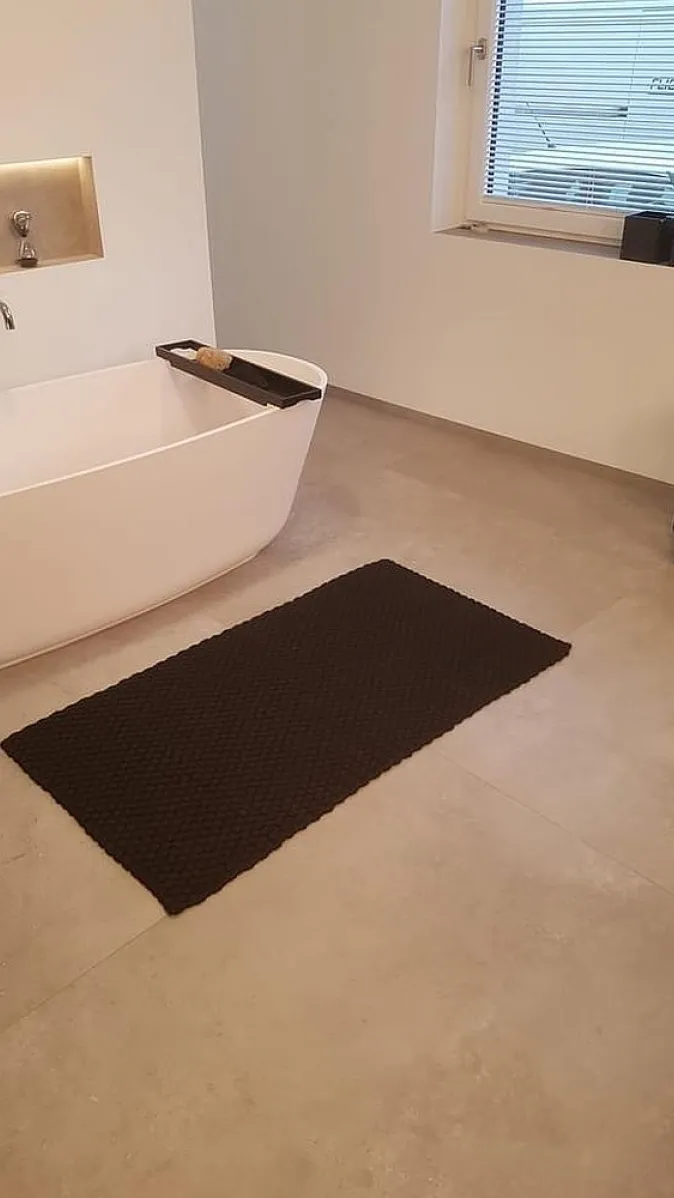 Badezimmer mit freistehender Wanne, schwarzem Teppich und kleiner Fensterbank mit Orchidee.