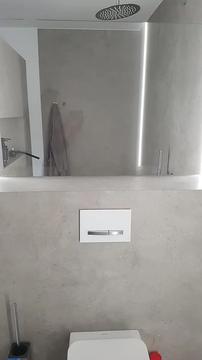 Minimalistisches WC mit Betonwand und silbernem Licht durch vertikale LED-Beleuchtung. 