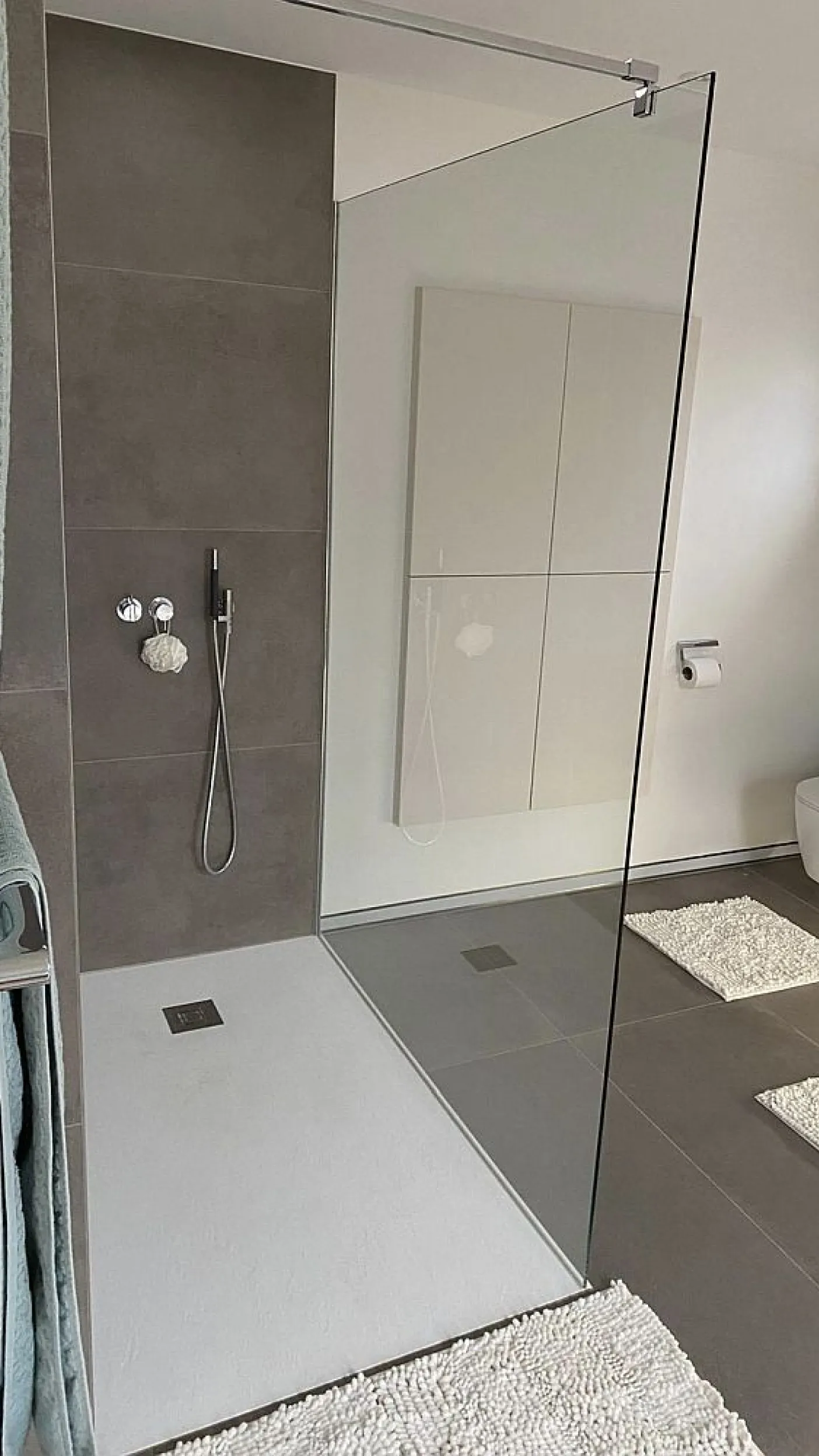 Eine bodengleiche, barrierefreie Dusche mit grauen Wandfliesen und einer Duschfläche in Weiß.