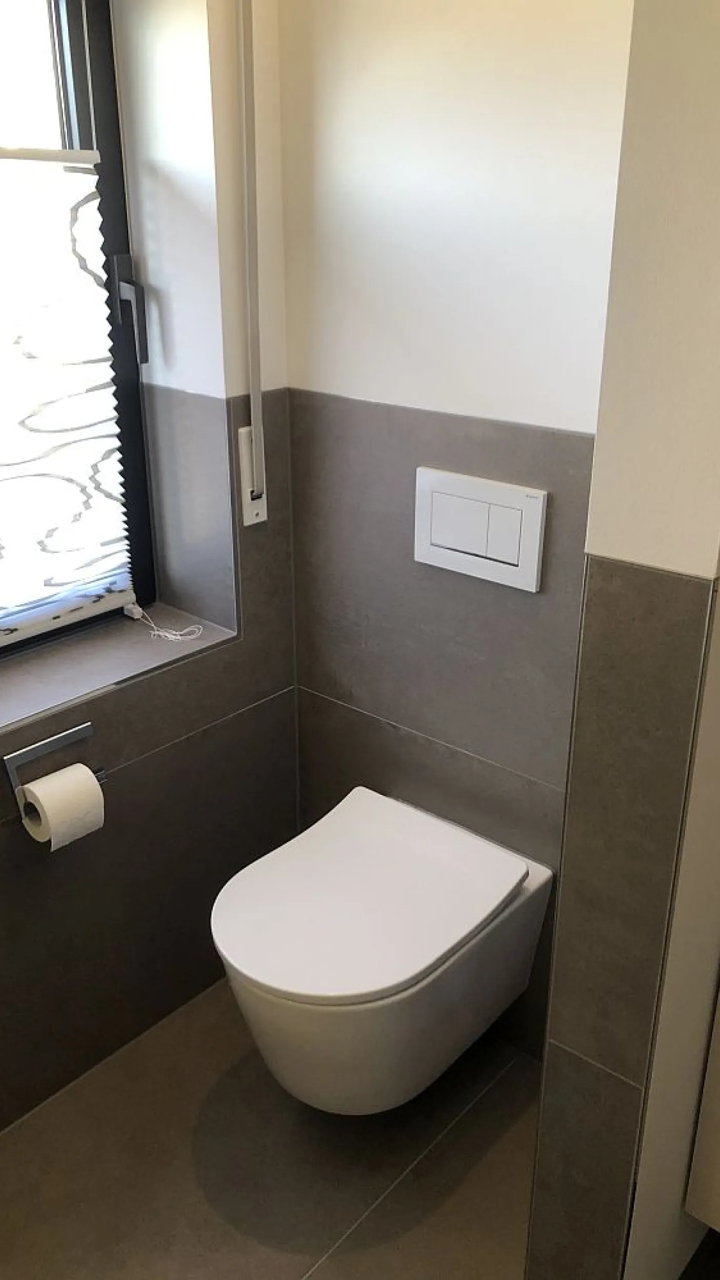 Ein modernes Gäste-WC mit einer hängenden Toilette und grauen Wandfliesen, die bis zur Hälfte der Wandhöhe reichen.