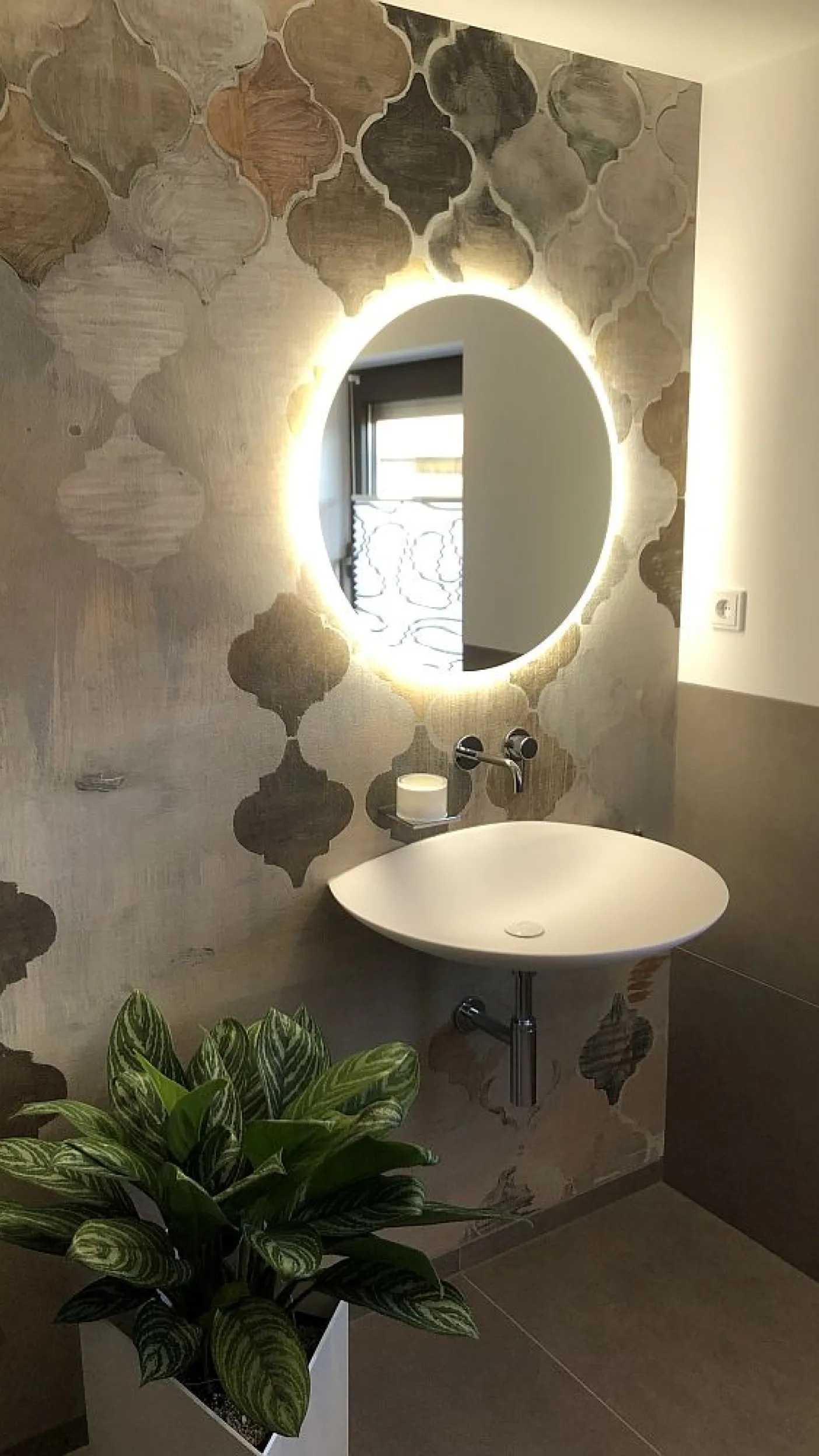 Ein kleiner Gäste-Waschtisch mit einem runden, hinterleuchteten Spiegel, der für ein angenehmes Licht sorgt.