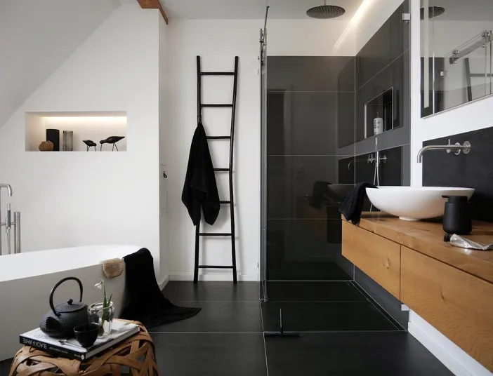 Helles Dachbad mit großzügiger Badewanne, schwarzem Dekor, Glasdusche, modernen Armaturen und Tageslicht, das durch ein schräges Dachfenster einfällt.