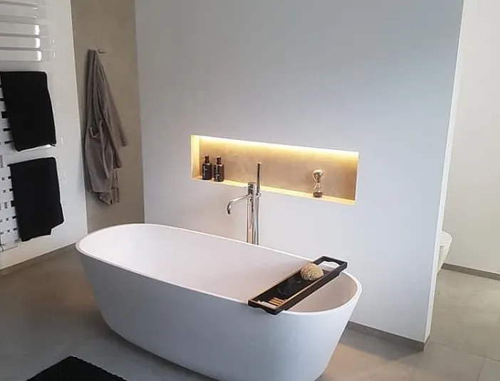 Stilvolle Badewanne mit goldener LED-Nische, Wandarmatur und schwarzem Teppich.