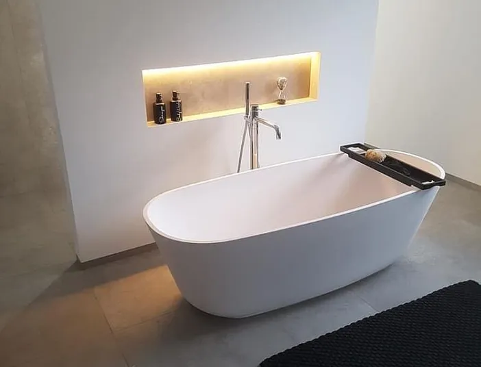 Freistehende Badewanne vor einer Wand mit golden beleuchteter Nische.
