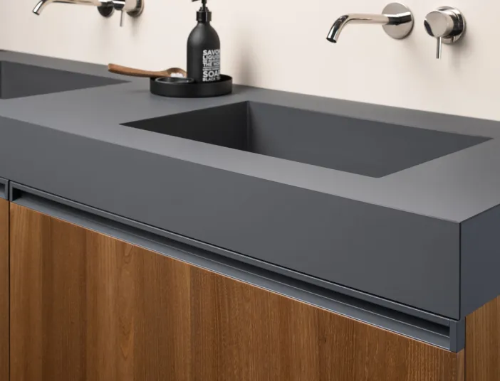 Detail eines Stocco Doppelwaschtisches mit integrierten Becken, dunkler Oberfläche und wandmontierten Armaturen.